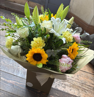 Sunlit - A radiant hand-tied bouquet inspired by warm summer days and joyful moments. Featuring a beautiful blend of sunshine-yellow, soft ivory, and delicate blush tones, this elegant arrangement is complemented by lush greenery and graceful seasonal textures for a naturally uplifting display.

Finished with stylish wrapping, a coordinating gift box, and a delicate decorative accent, this bouquet is perfect for birthdays, celebrations, thank-you gifts, new baby occasions, or simply bringing a little sunshine into someone's day.