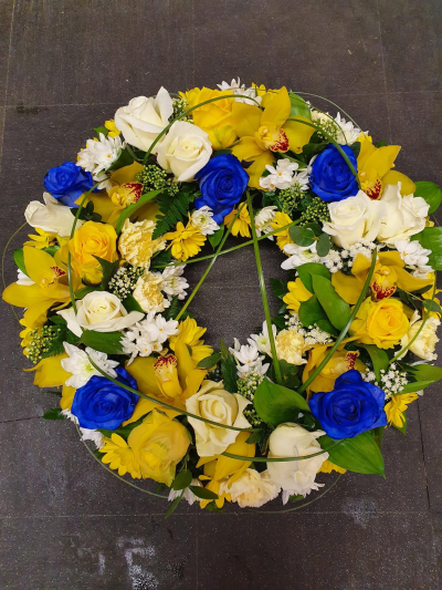 Vibrant Wreath - A striking funeral wreath designed in radiant shades of gold, ivory, and vibrant blue, symbolising cherished memories, enduring love, and a life beautifully lived. The circular design represents eternity and the unbroken bond shared with those we hold dear, while the uplifting colour palette offers a heartfelt tribute filled with warmth and remembrance.

Expertly handcrafted, this elegant wreath creates a meaningful focal point for funeral services, memorial ceremonies, or celebrations of life, expressing sympathy, respect, and lasting affection.